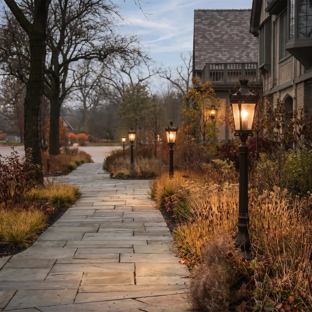 Lamp post light fixture lining a stone garden path beside a house with warm glowing lanterns.