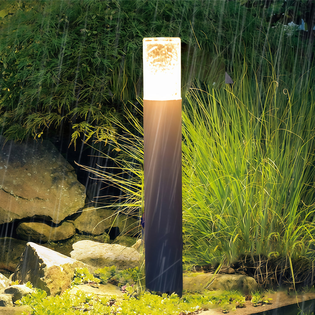 Slim dark landscape bollard light fixtures glowing along a garden edge, enhancing nighttime visibility.