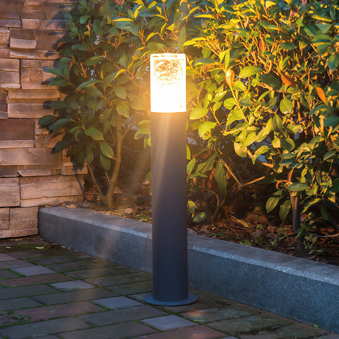 Modern landscape bollard light fixtures illuminating a garden pathway with bright vertical light.