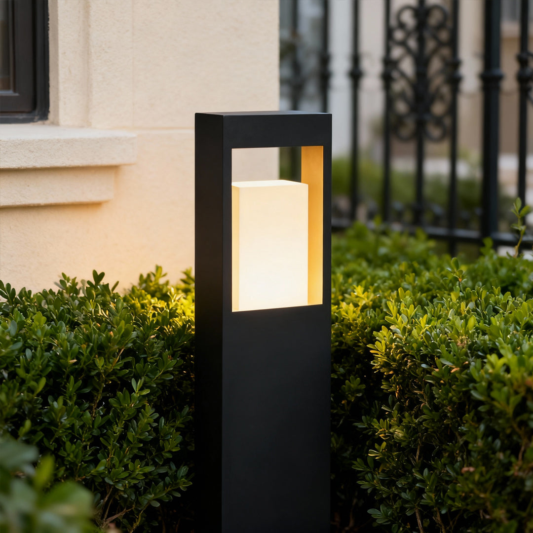 Landscape bollard lighting installed in garden shrubs, featuring a tall black frame and inviting warm glow.