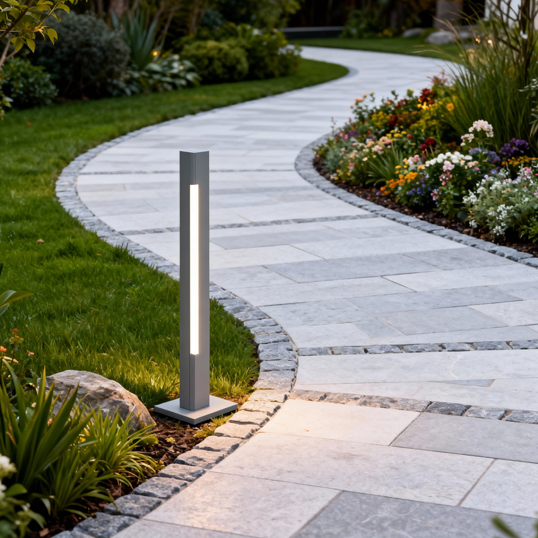 Modern landscaped yard scene showcasing bronze led bollard light fixtures illuminating rocks and greenery.