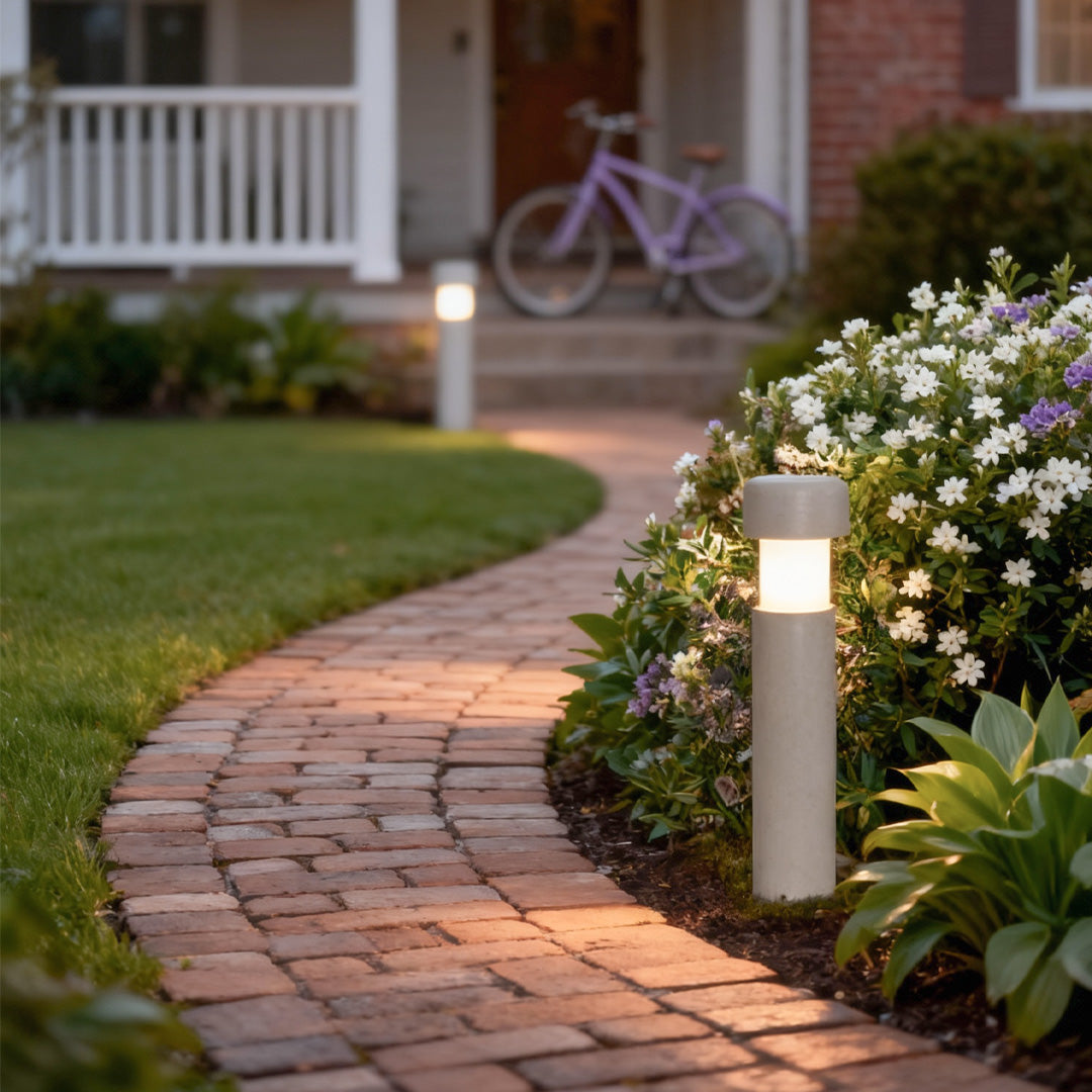 White-top landscape lighting bollards lining a residential brick pathway, providing warm ambient path lighting.
