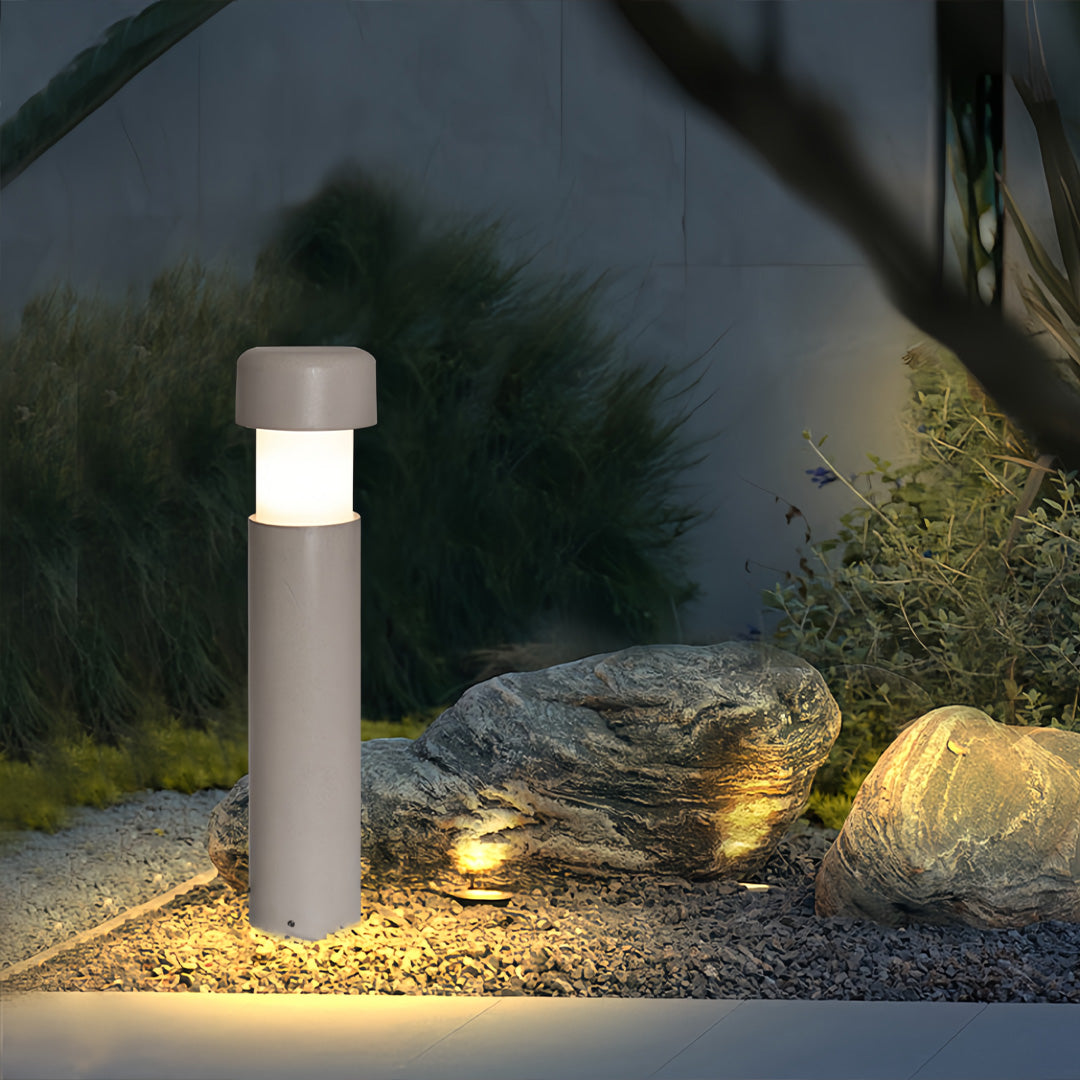 Landscape lighting bollards installed along a nighttime garden walkway, casting warm illumination on surrounding plants.