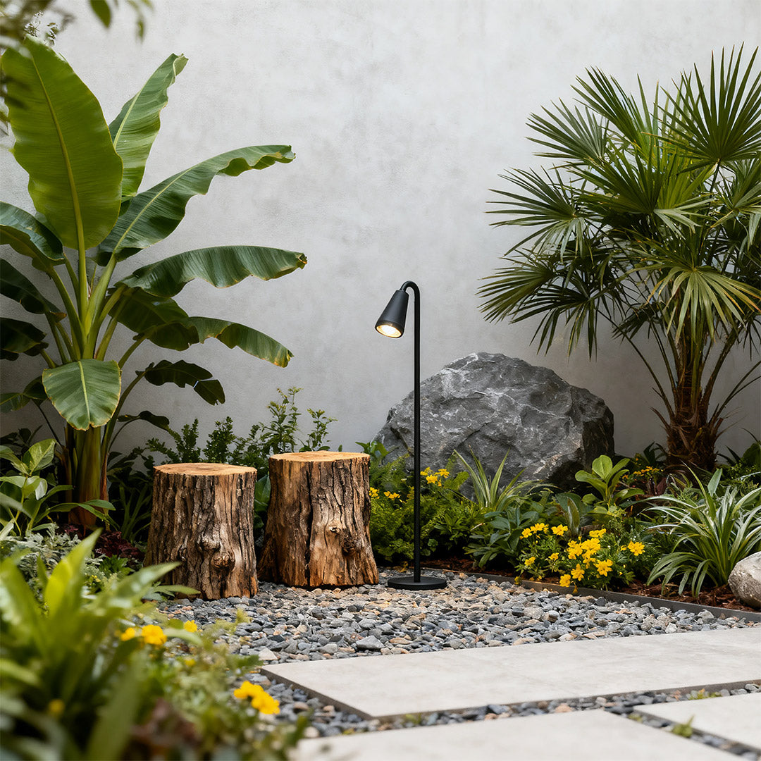Landscape path light placed near a tree stump and colorful flowers, enhancing the garden's ambiance.