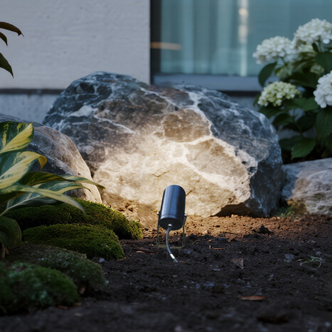 Landscape lighting spotlights creating dramatic accent illumination on decorative rock formation in garden setting