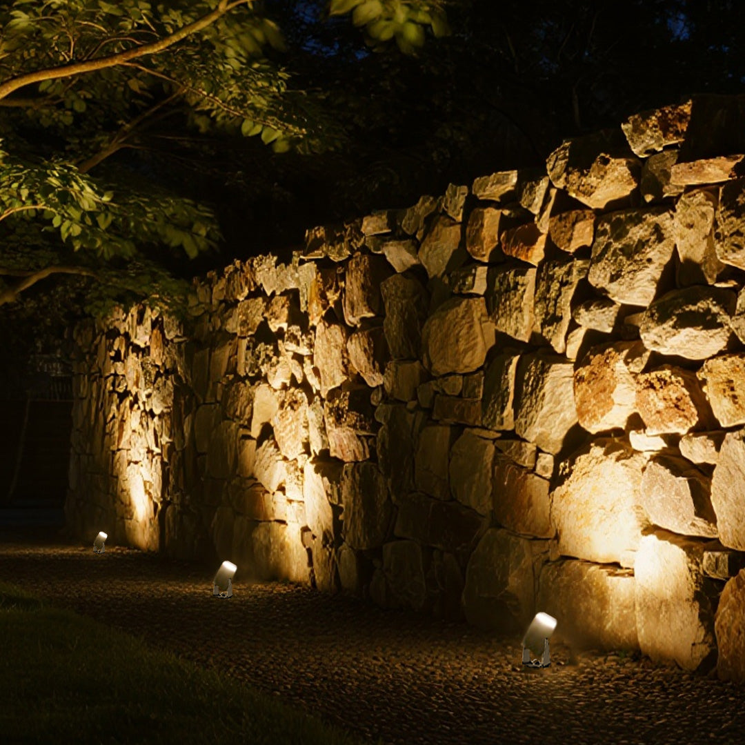 Landscape lighting spotlights creating warm uplighting effect on mature tree trunks in evening garden setting