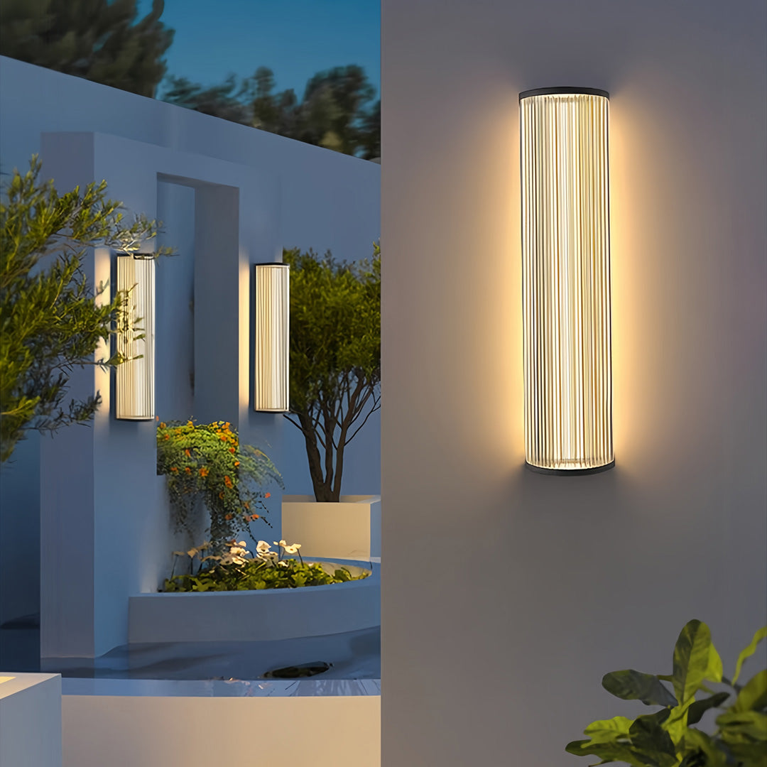 Landscape with two vertical wall sconce lighting fixtures highlighting exterior walls and garden features at night.