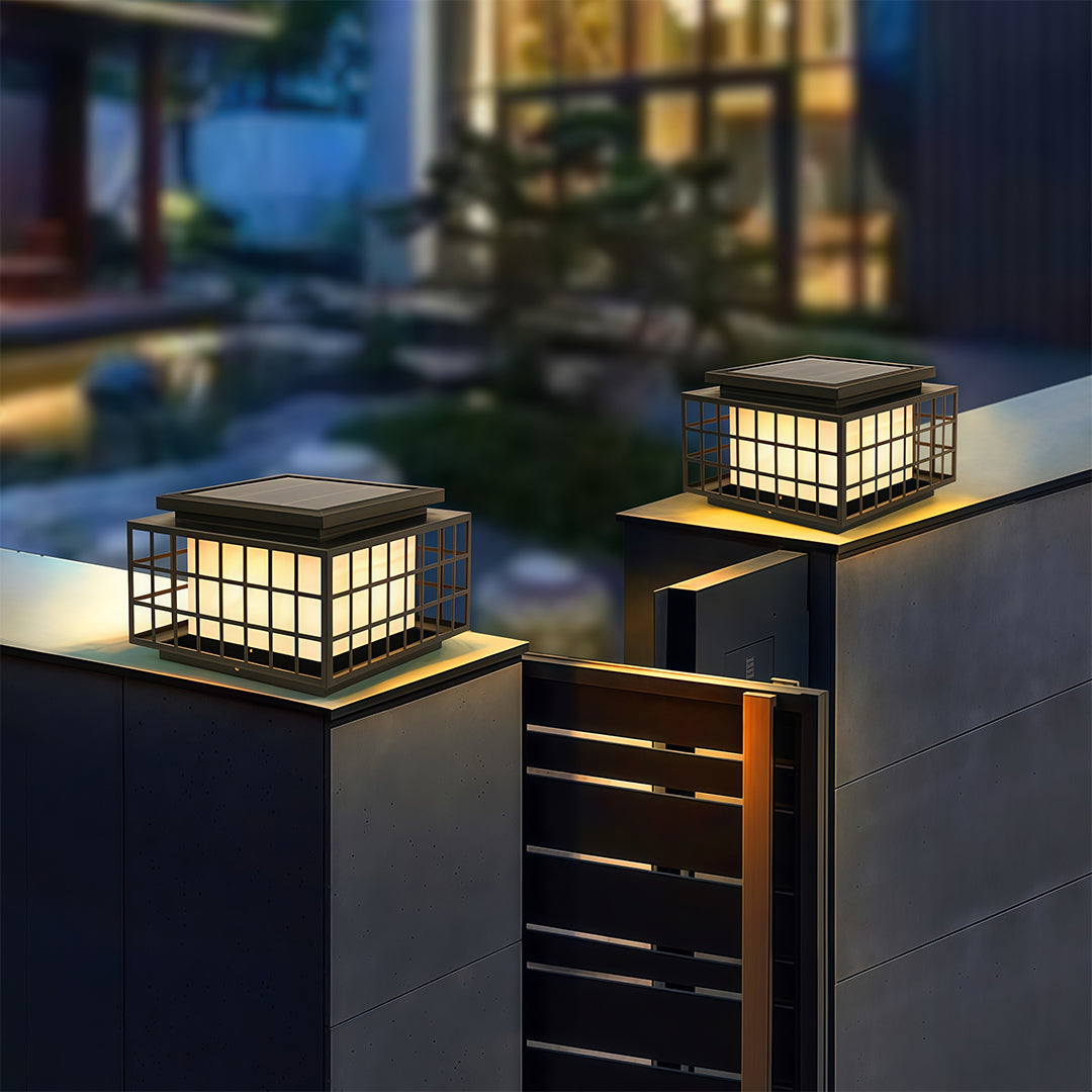 Modern gate pillar lights with a black metal frame, installed in a landscaped garden for aesthetic appeal.