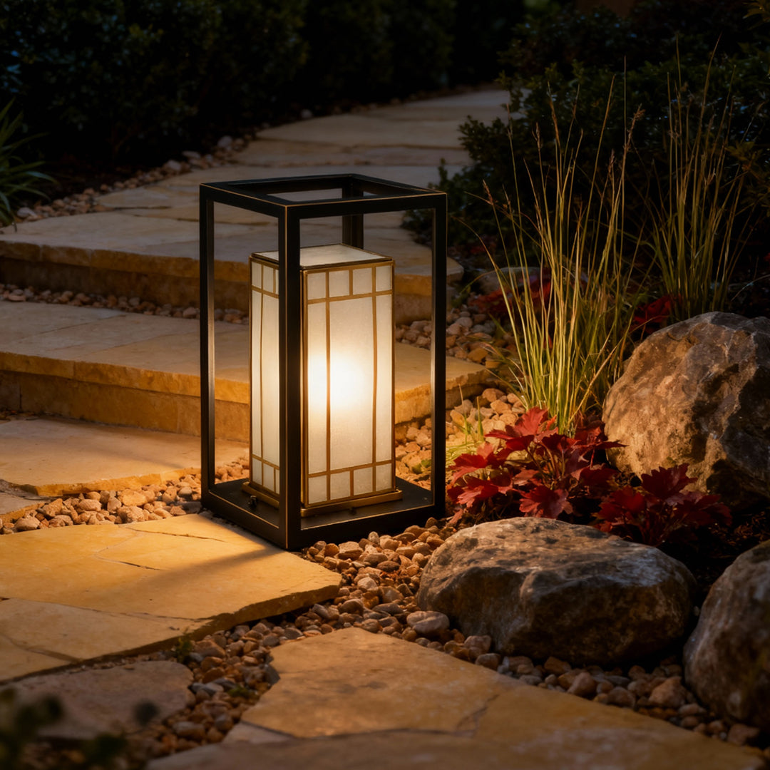 Lantern bollard light positioned near shrubs and rocks, casting a warm glow that enhances garden textures after dark.