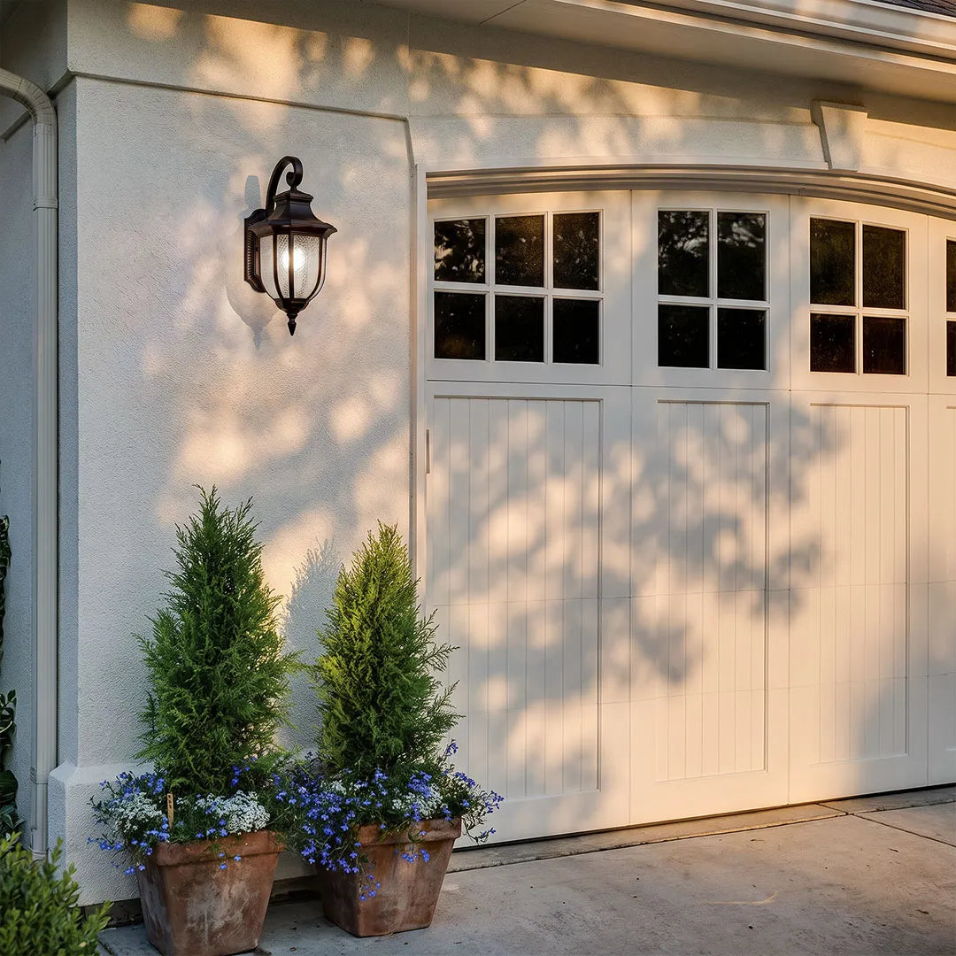 Lantern outdoor wall lights casting decorative shadows beside a garage and outdoor planting area.