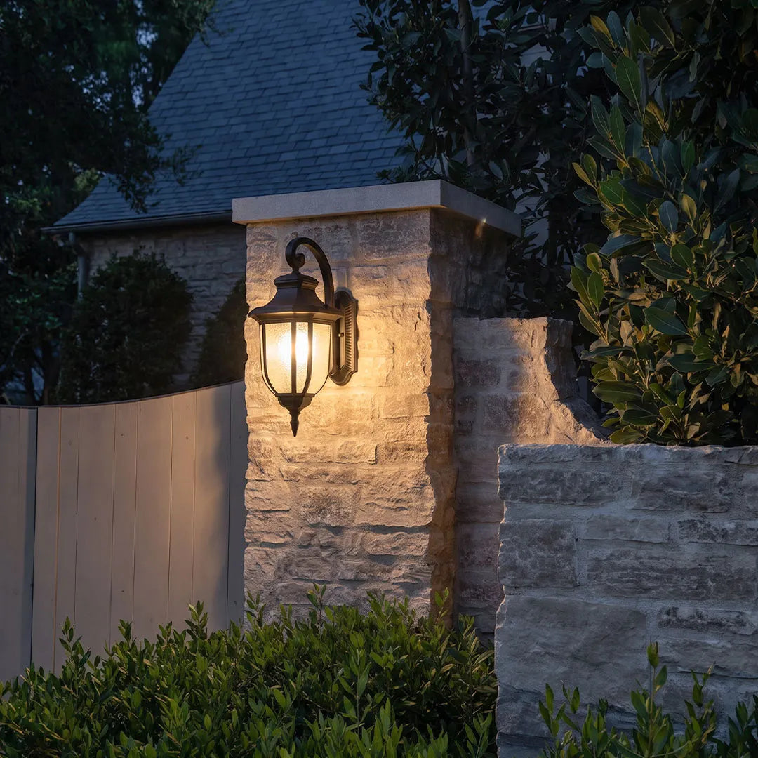 Lantern outdoor wall lights mounted on a stone entrance pillar for warm nighttime landscape lighting.