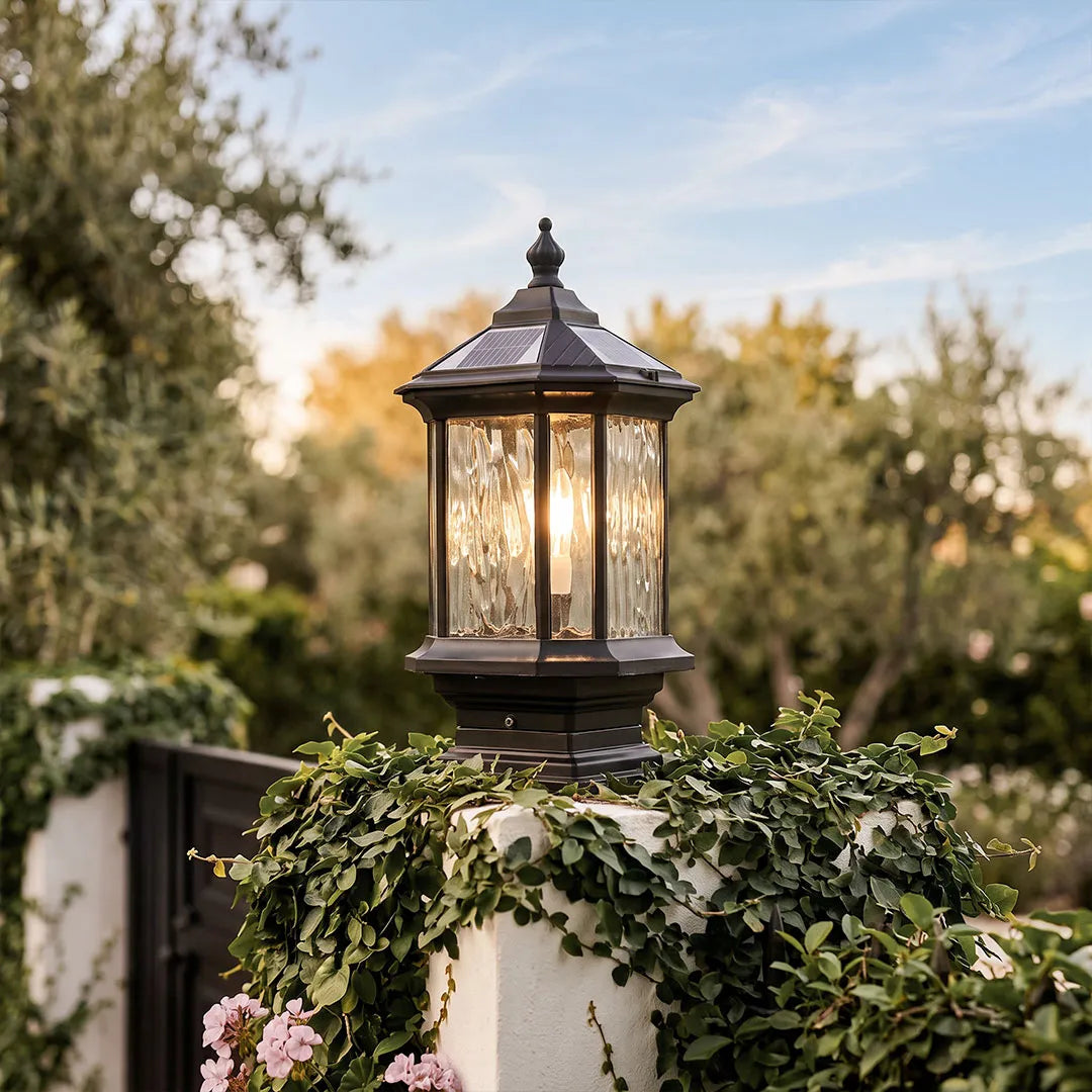 Lantern pillar light mounted on a stone gate post with greenery and warm illumination.