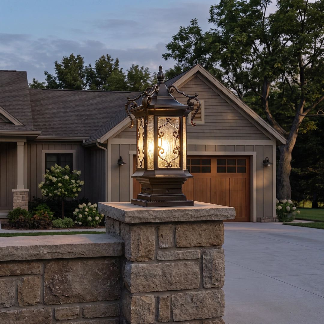 Lantern pillar lights mounted on a stone pillar at the end of a driveway near a garage and landscaped path.