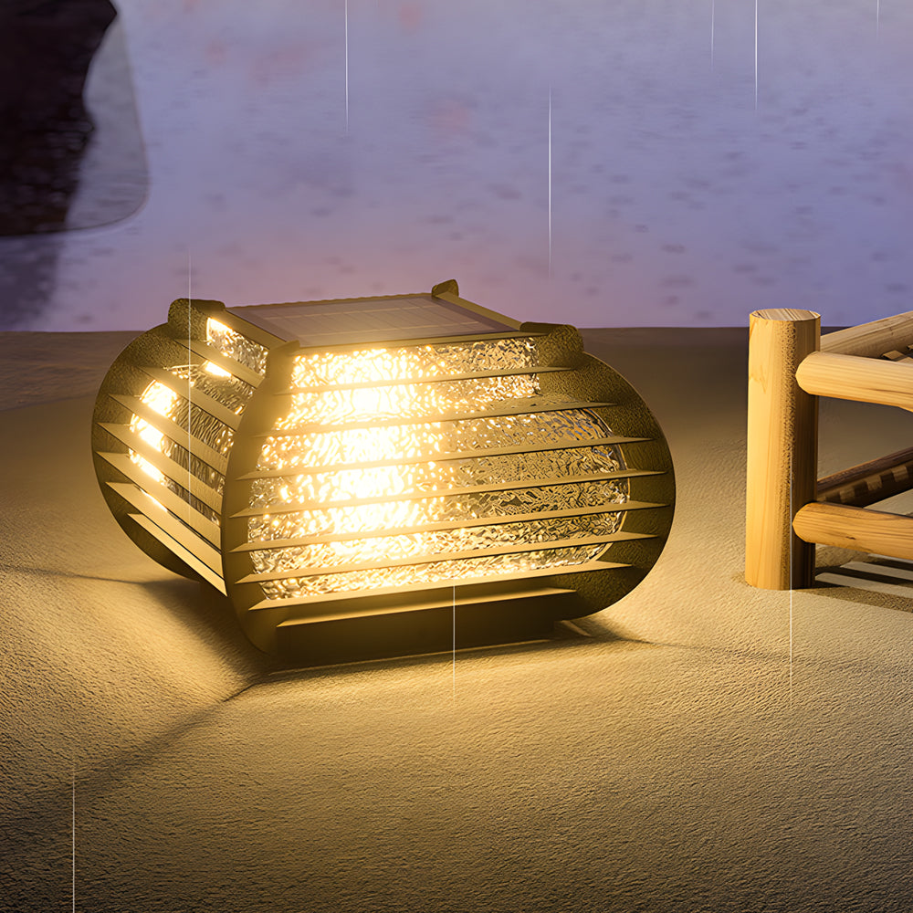 Modern lantern pillar lights resting on the ground, casting warm light across a minimalist outdoor patio area.