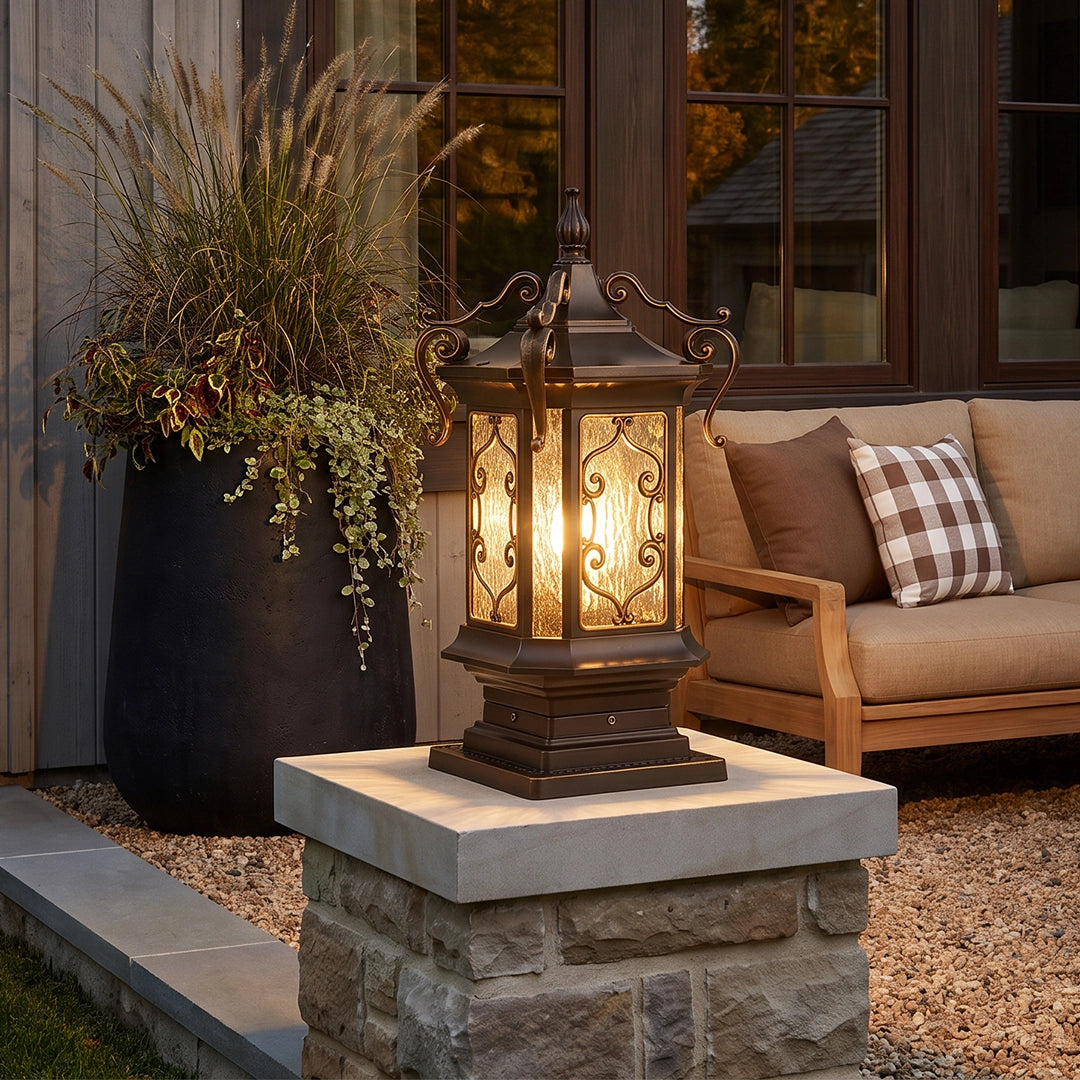 Lantern pillar lights placed on a concrete pedestal beside an outdoor seating area with warm ambient lighting.