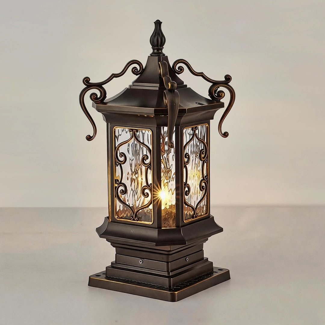 Lantern pillar lights product view showing an ornate bronze post light with curled metal accents and textured glass.