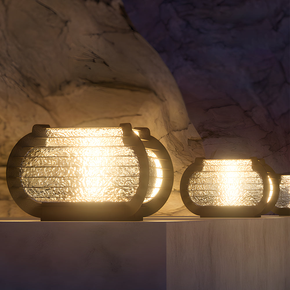 Decorative lantern pillar lights set against a stone wall, emitting soft ambient light for modern garden spaces.