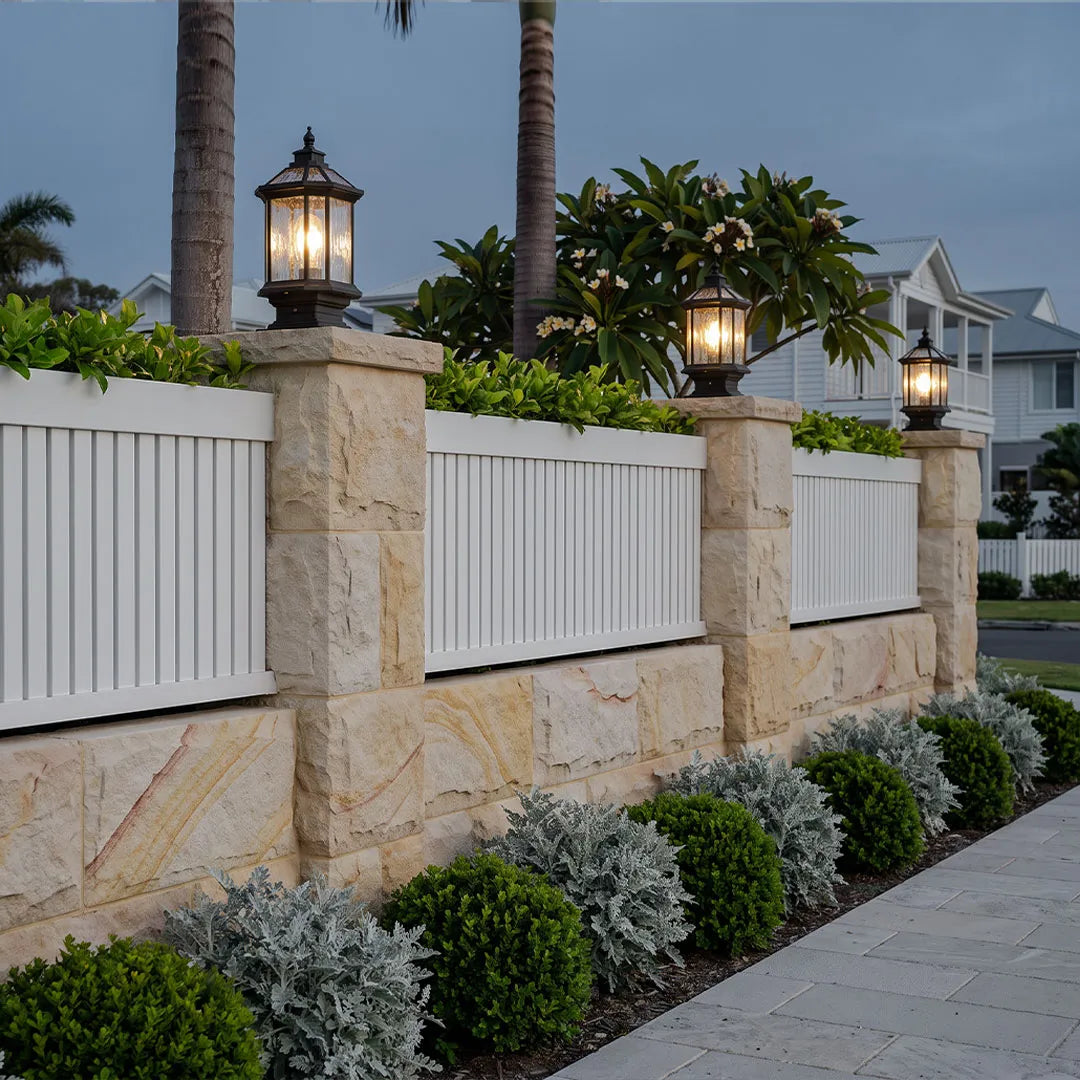 Lantern pillar lights installed along a white fence on stone columns in a front yard.
