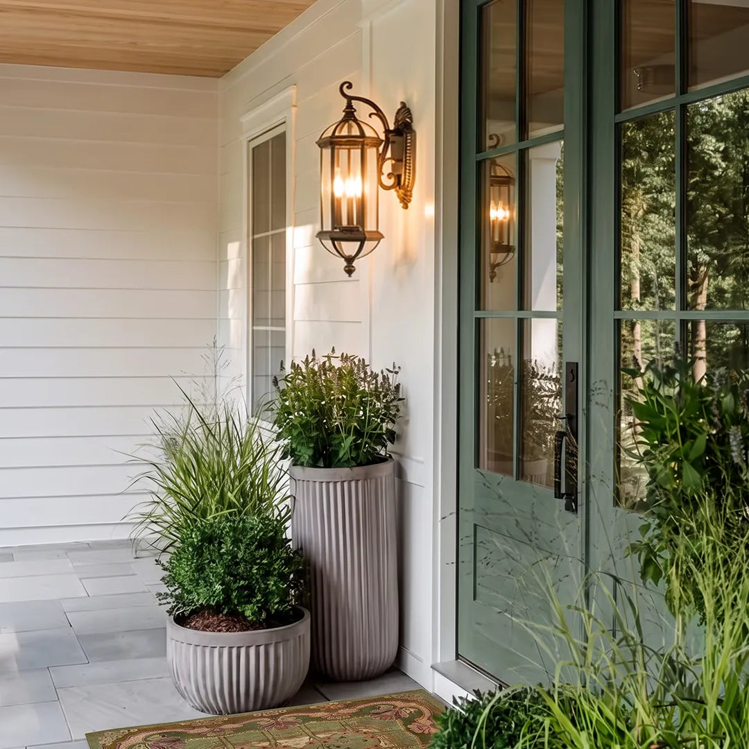 Lantern style outdoor wall light mounted beside a front door with planters, highlighting a welcoming exterior entrance.