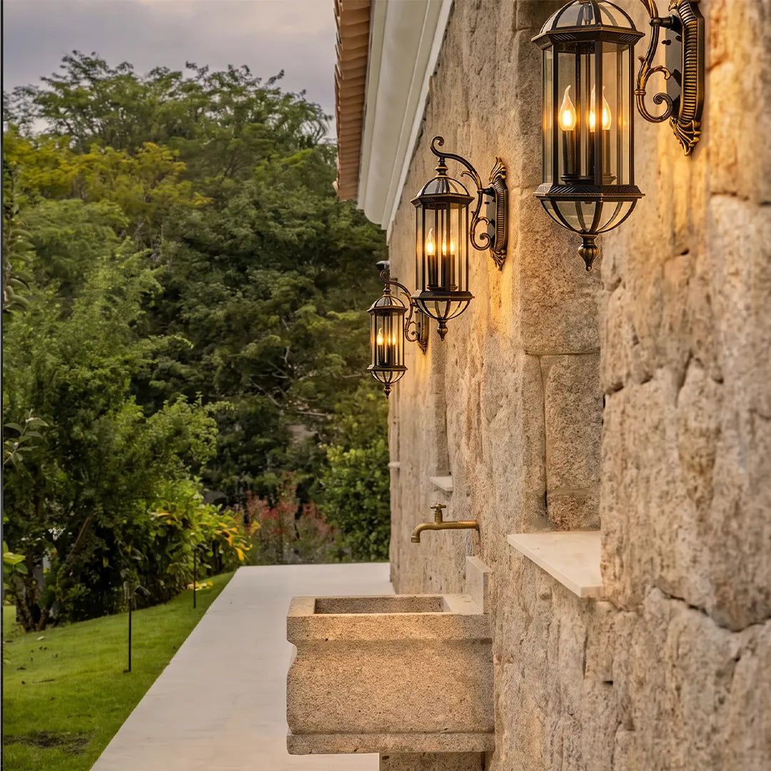 Lantern style outdoor wall lights mounted along a stone exterior walkway, creating a warm and elegant architectural lighting effect.