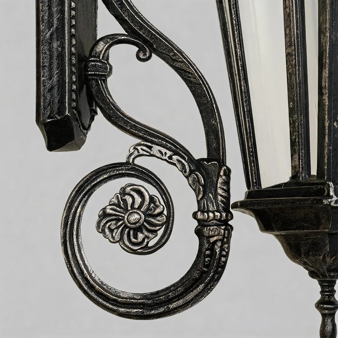 Lantern style wall sconce detail highlighting the decorative scroll arm and ornate vintage metal craftsmanship.