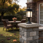 Elegant large black outdoor pillar light illuminating a cozy garden patio with stone pillars and wicker furniture.