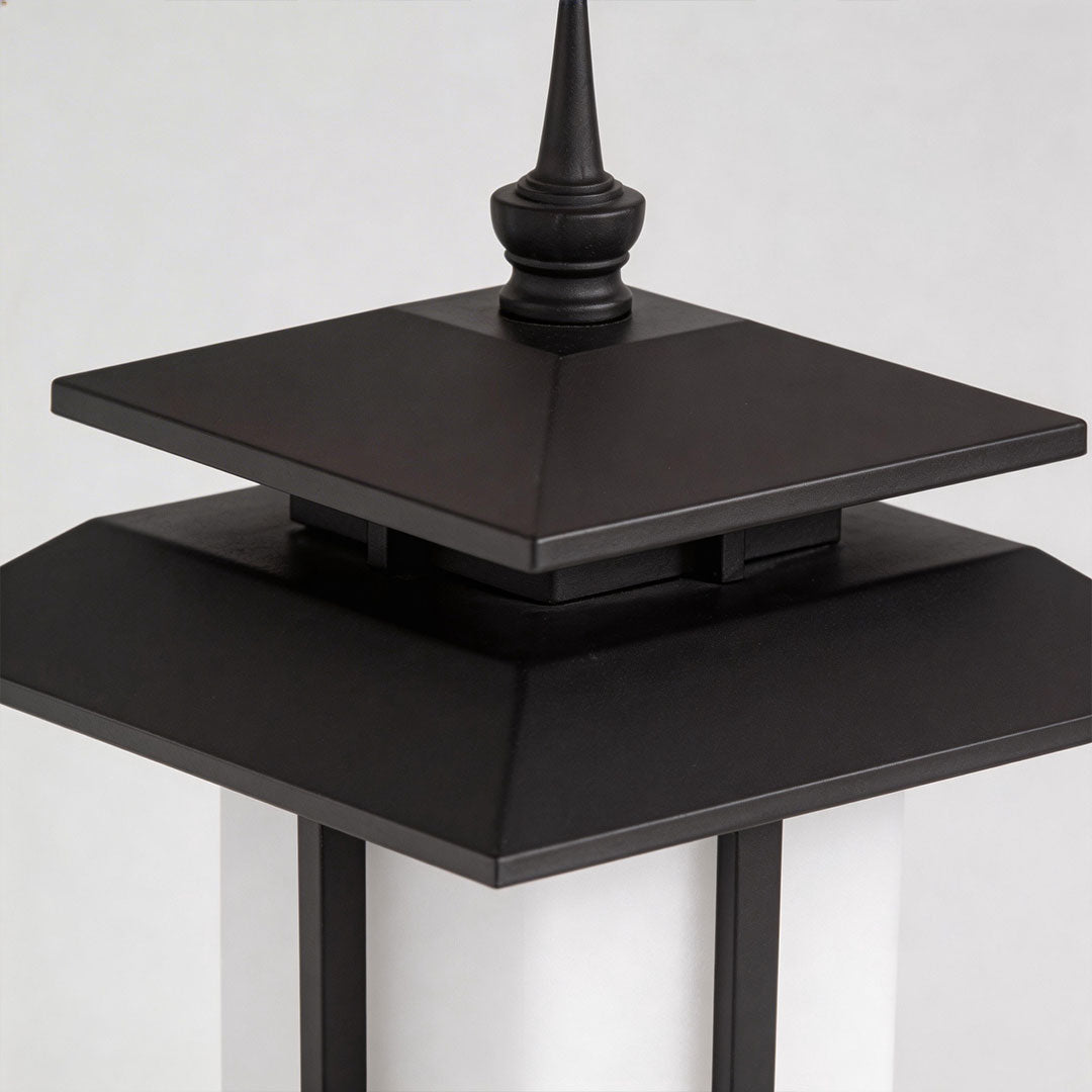 Close-up of a large black outdoor pillar light top with intricate design and pointed roof.