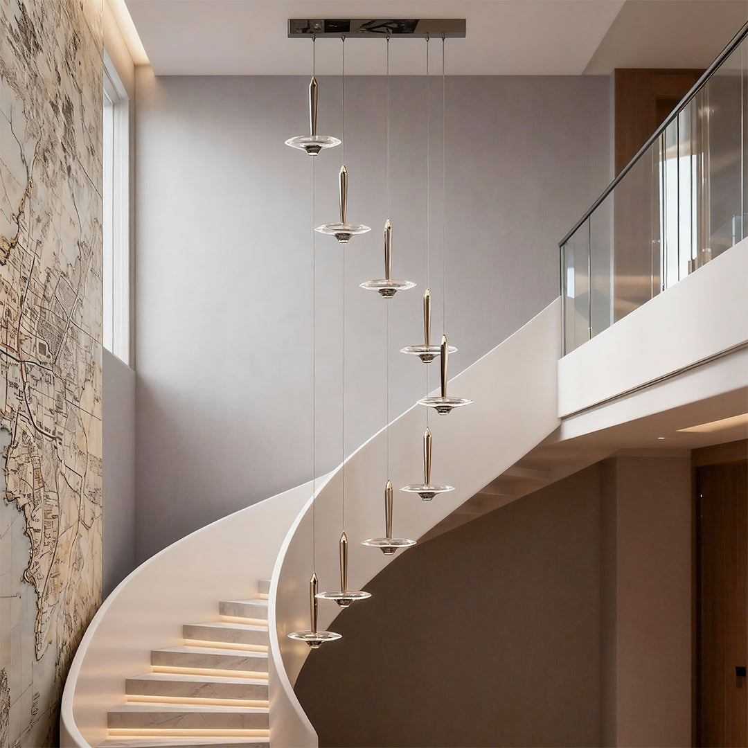 Large crystal pendant light descending beside spiral staircase in luxury space with stone column architectural details