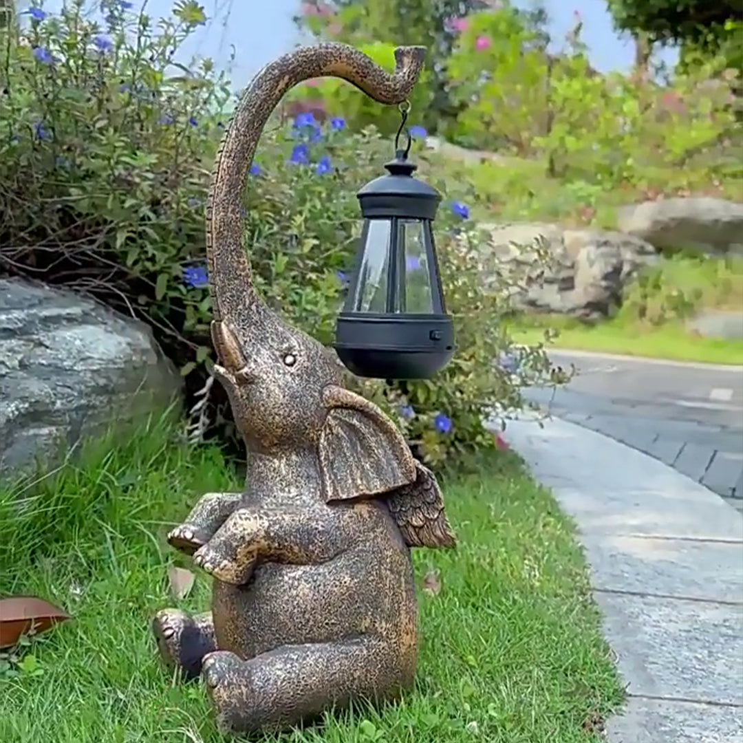 Large elephant garden ornament with hanging lantern placed on stone pathway in landscaped area