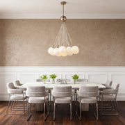Large modern bubble glass chandelier featuring multiple frosted white orbs, centered over a long gray dining table in a textured room.