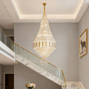 Large gold chandelier illuminating grand foyer with double-height ceiling and marble staircase.