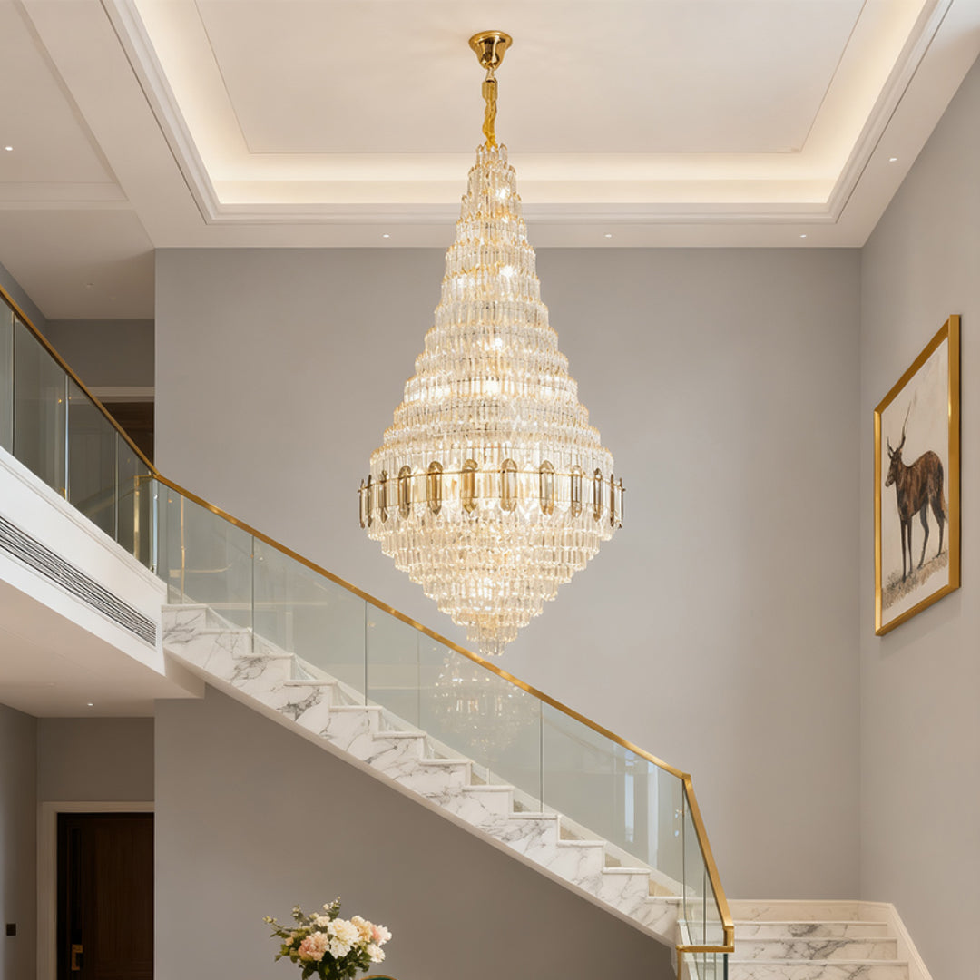 Large gold chandelier illuminating grand foyer with double-height ceiling and marble staircase.