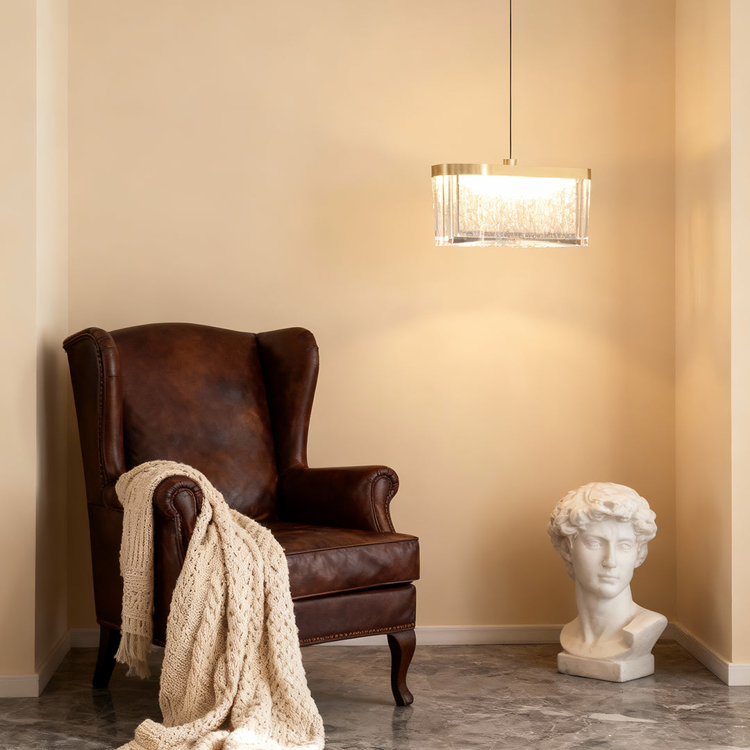 Large metal pendant lights illuminating cozy corner with vintage burgundy chair and classical bust sculpture decor