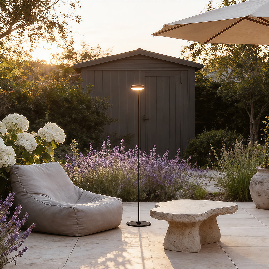 Stylish large outdoor pillar light mounted on a stone pillar beside a gated driveway at dusk.