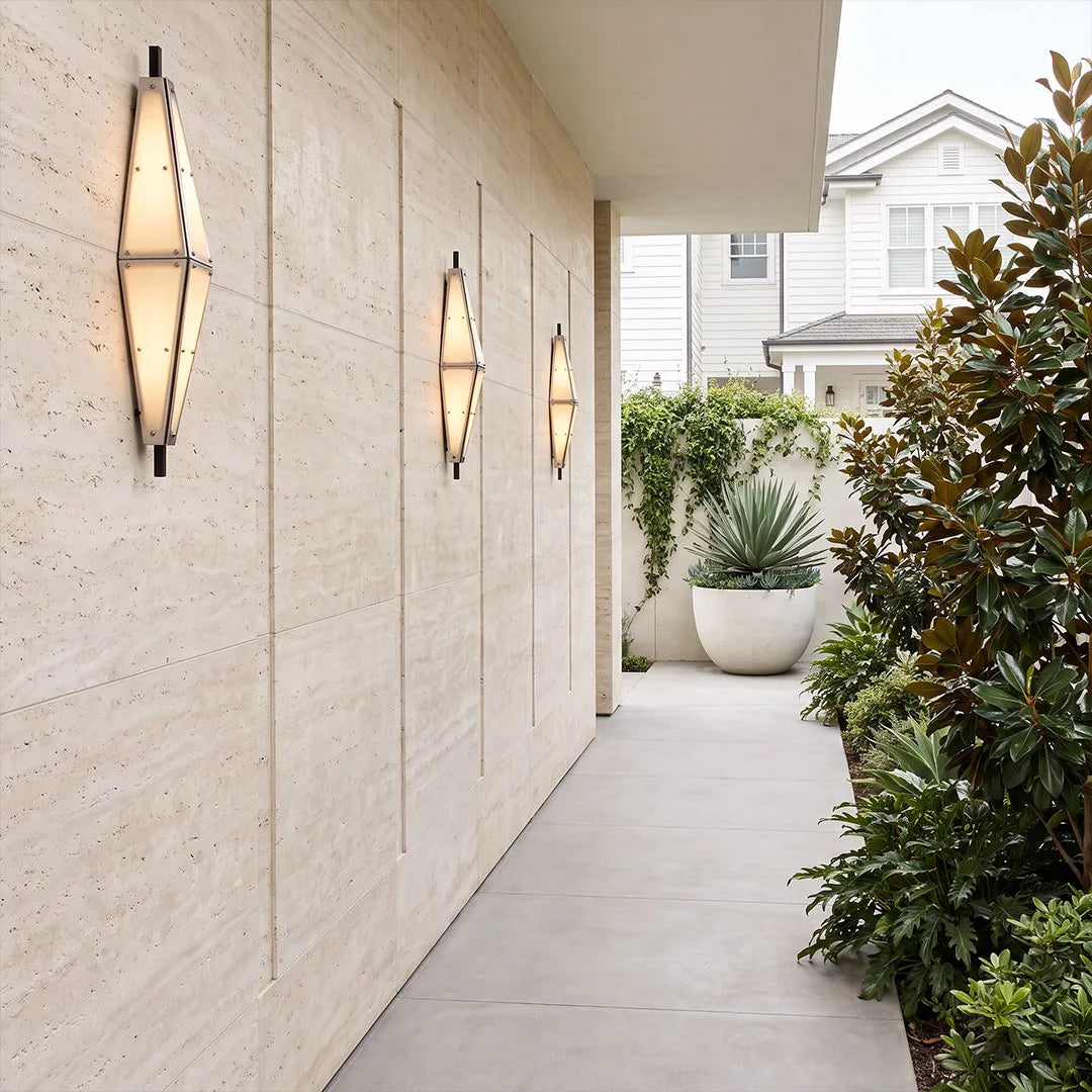 Large outdoor sconces arranged along a light stone exterior wall beside a narrow walkway.