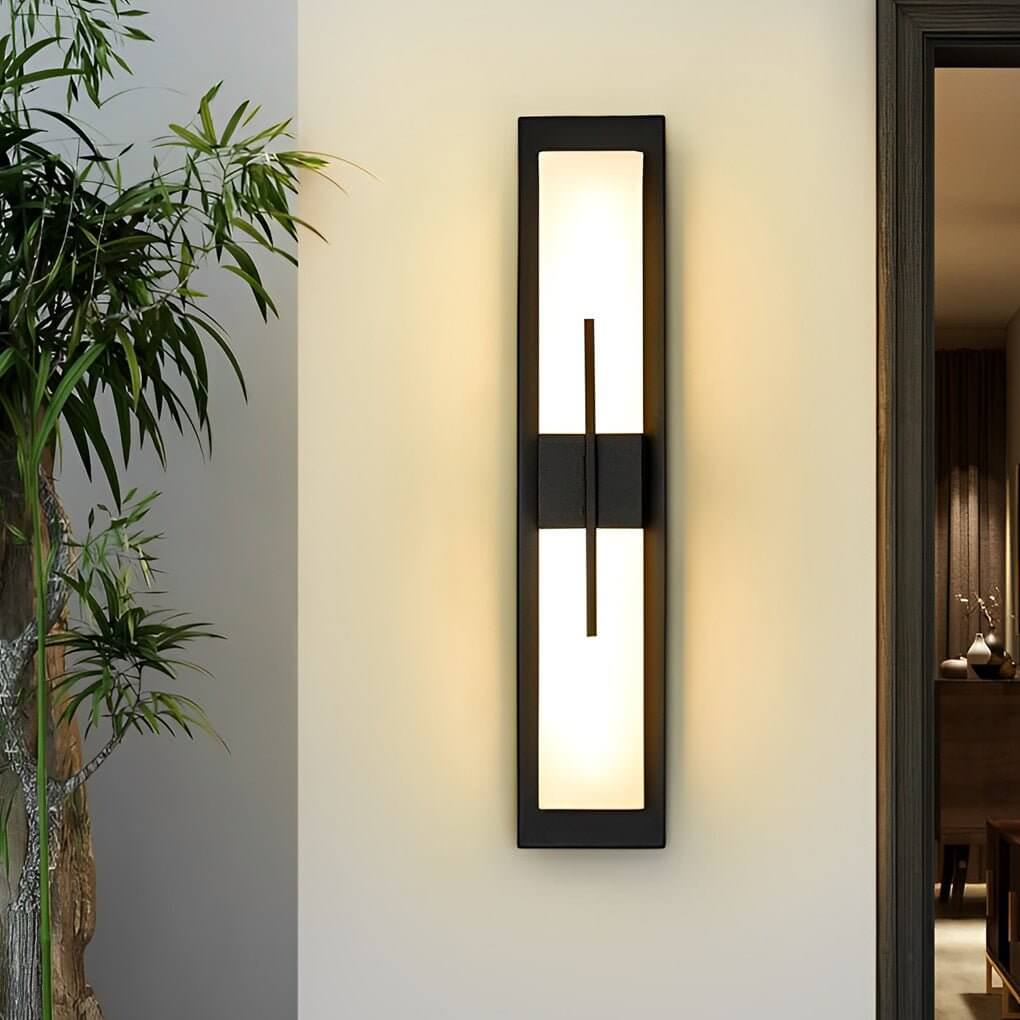 Large outdoor wall light fixture with black frame, casting soft light near a garden.