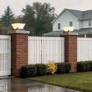 Large pillar lights installed on brick pillars beside a white picket fence and lush garden.