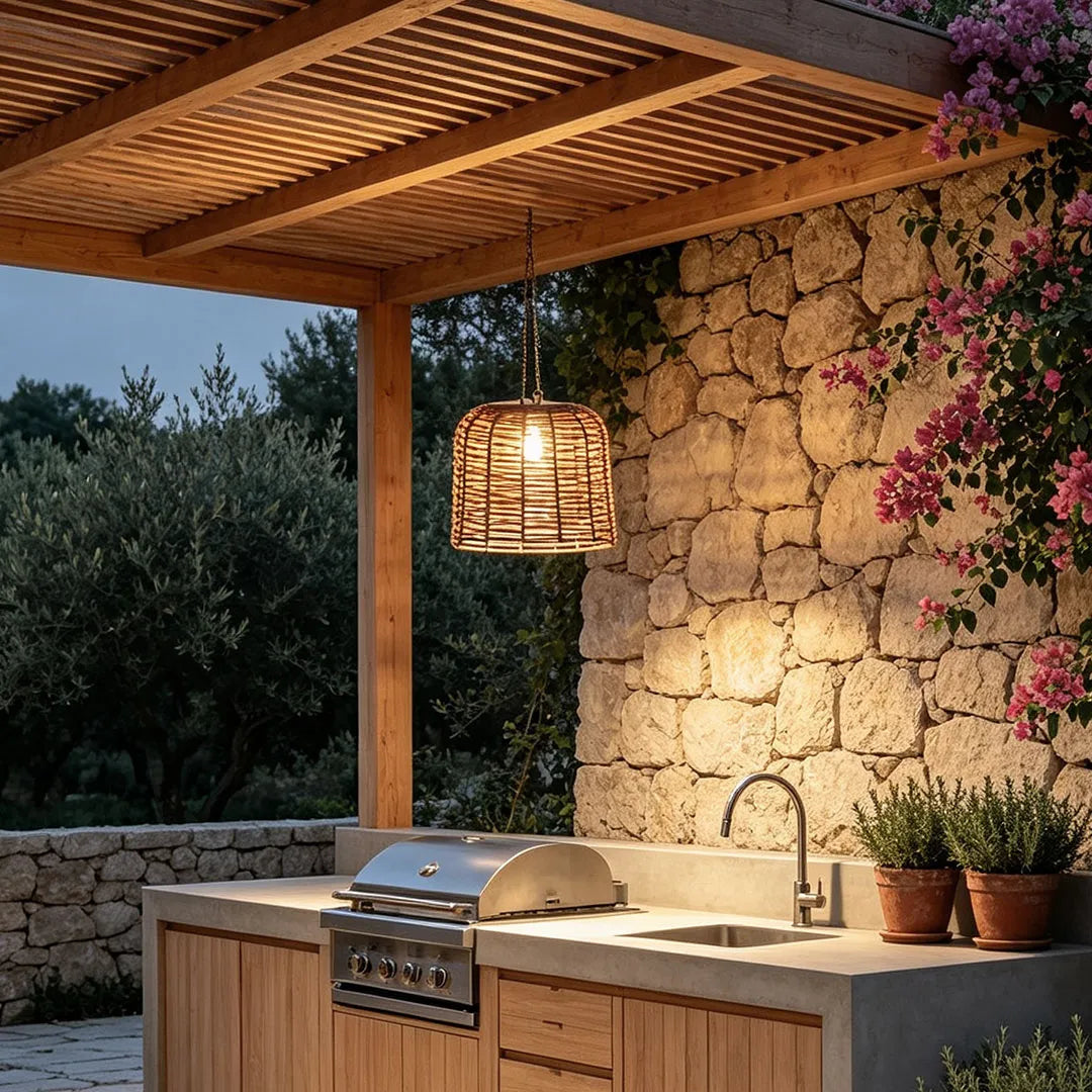 Large woven pendant light illuminating an outdoor kitchen beneath a wooden pergola beside a rustic stone wall.