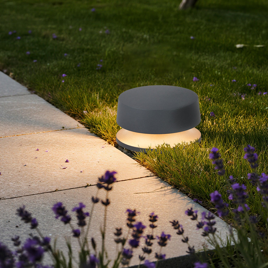 Circular LED path light illuminating lawn edge next to concrete walkway with warm ambient glow