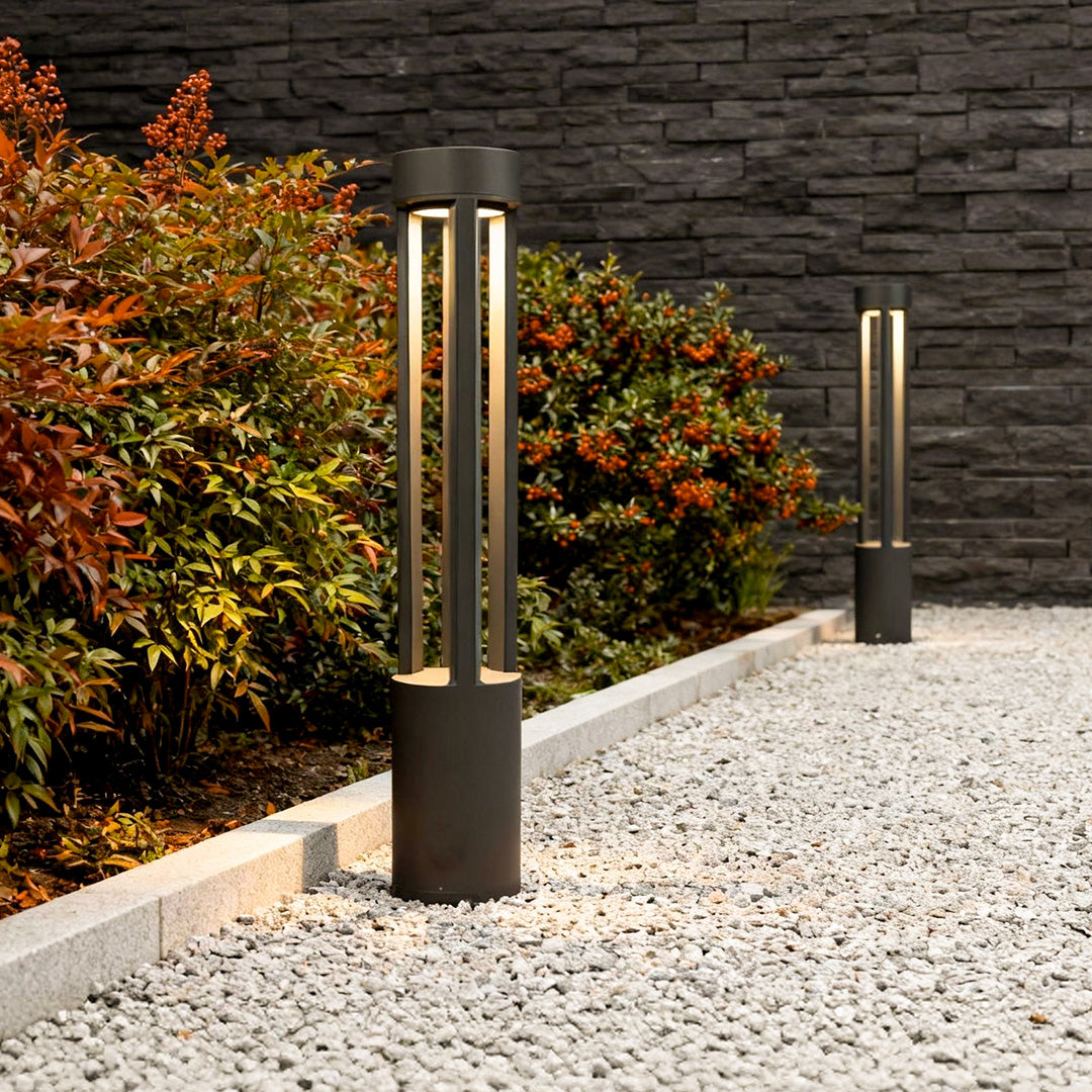 LED bollard path lights installed along a gravel garden walkway, featuring a slim black post with vertical light panels for outdoor pathways.