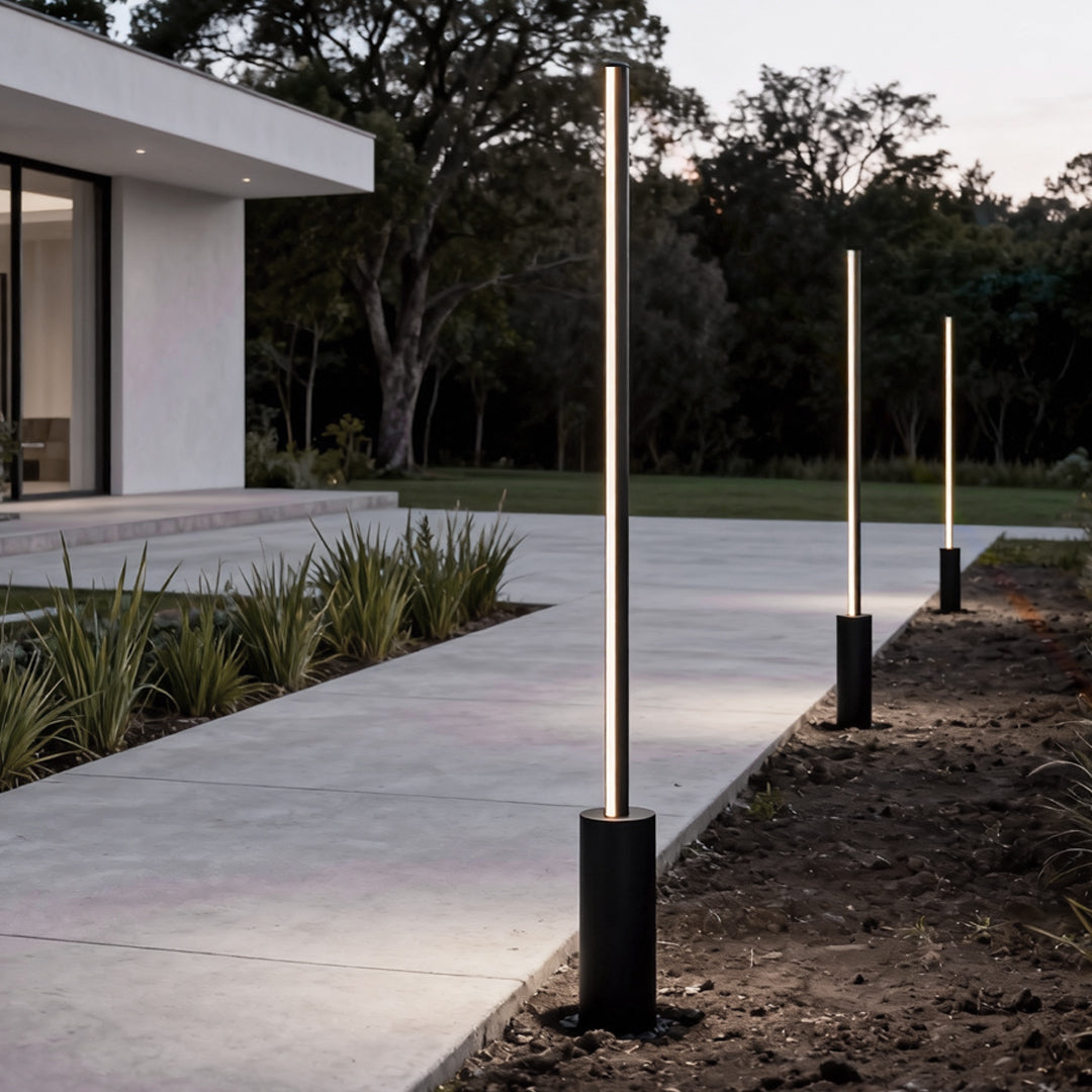 Slim contemporary outdoor floor lamps installed along a contemporary outdoor walkway at dusk.