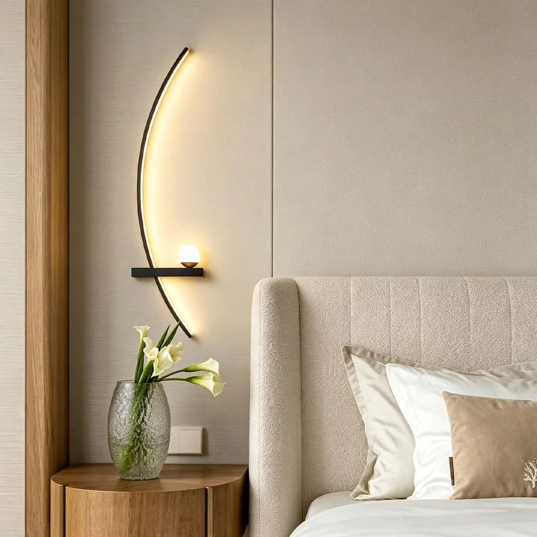LED curved wall light mounted beside a bed, featuring a slim glowing arc and a small accent globe.