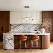LED infinity chandelier above a marble kitchen island with warm wood cabinetry in a modern interior.