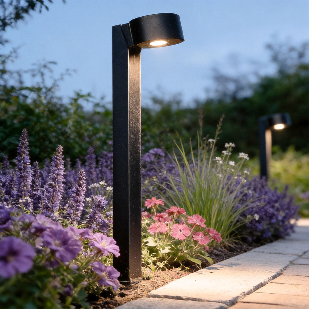 LED landscape path lighting installed beside blooming flowers, illuminating a curved garden walkway at dusk.