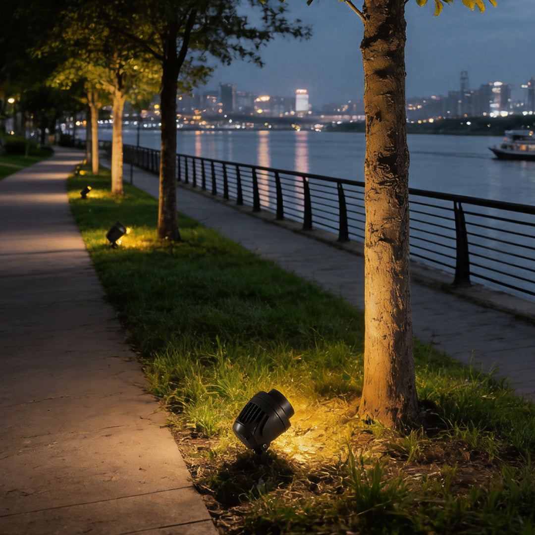 LED landscape spotlight illuminating riverside trees along a nighttime walkway.