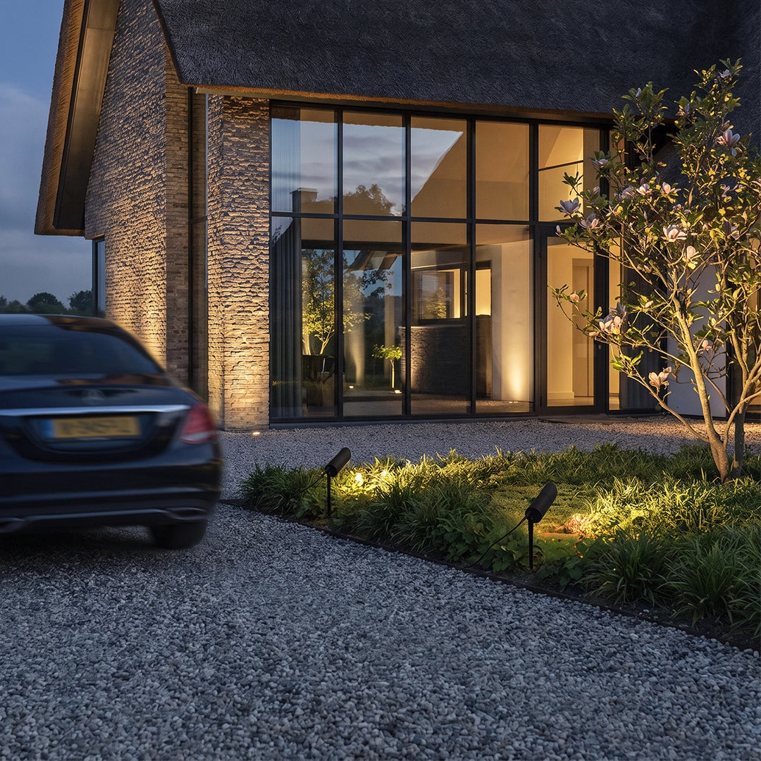 LED landscape spotlights lighting a gravel driveway and garden beside a modern house.