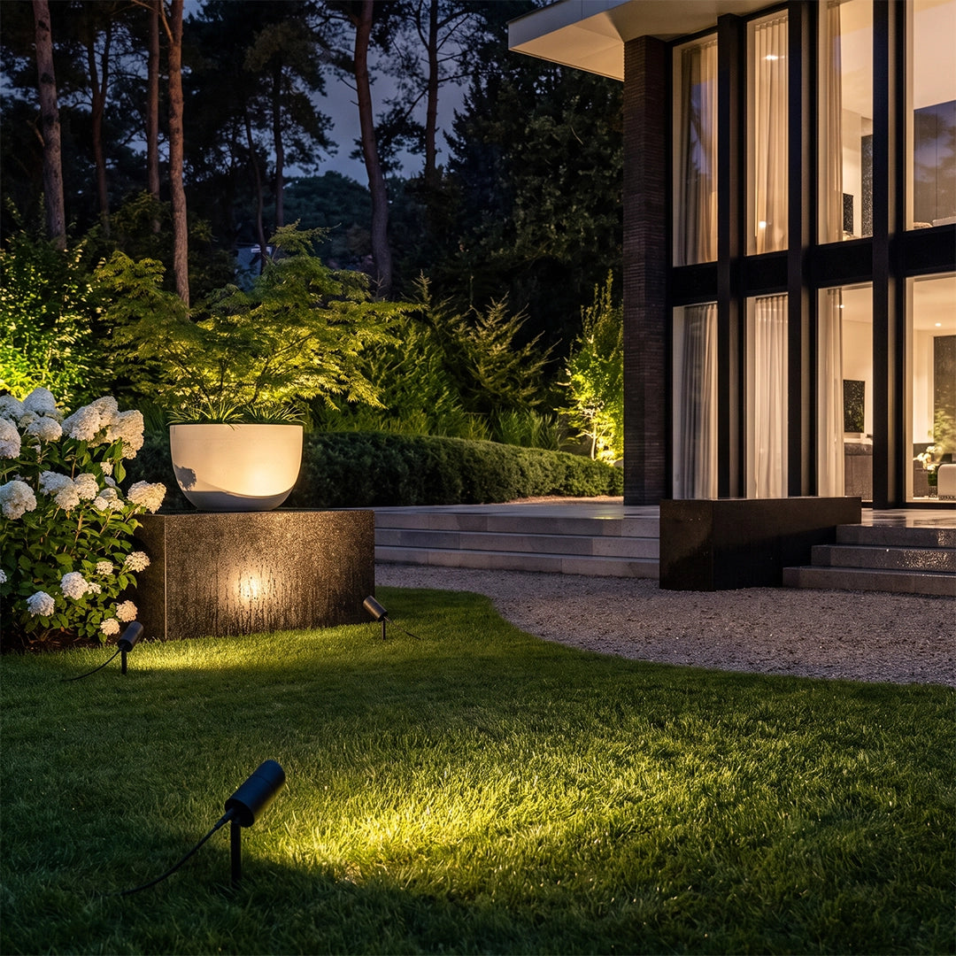 LED landscape spotlights brightening a lawn and garden bed beside a modern home at night.