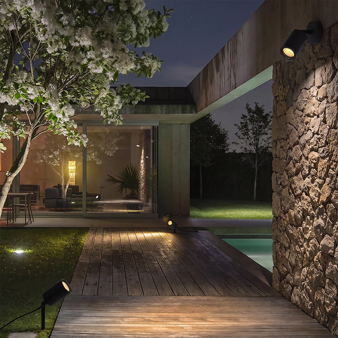 LED landscape spotlights lighting a poolside path and stone wall in a modern outdoor space.