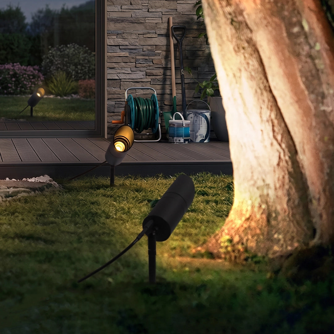 LED landscape spotlights illuminating a tree trunk and lawn beside a deck at night.