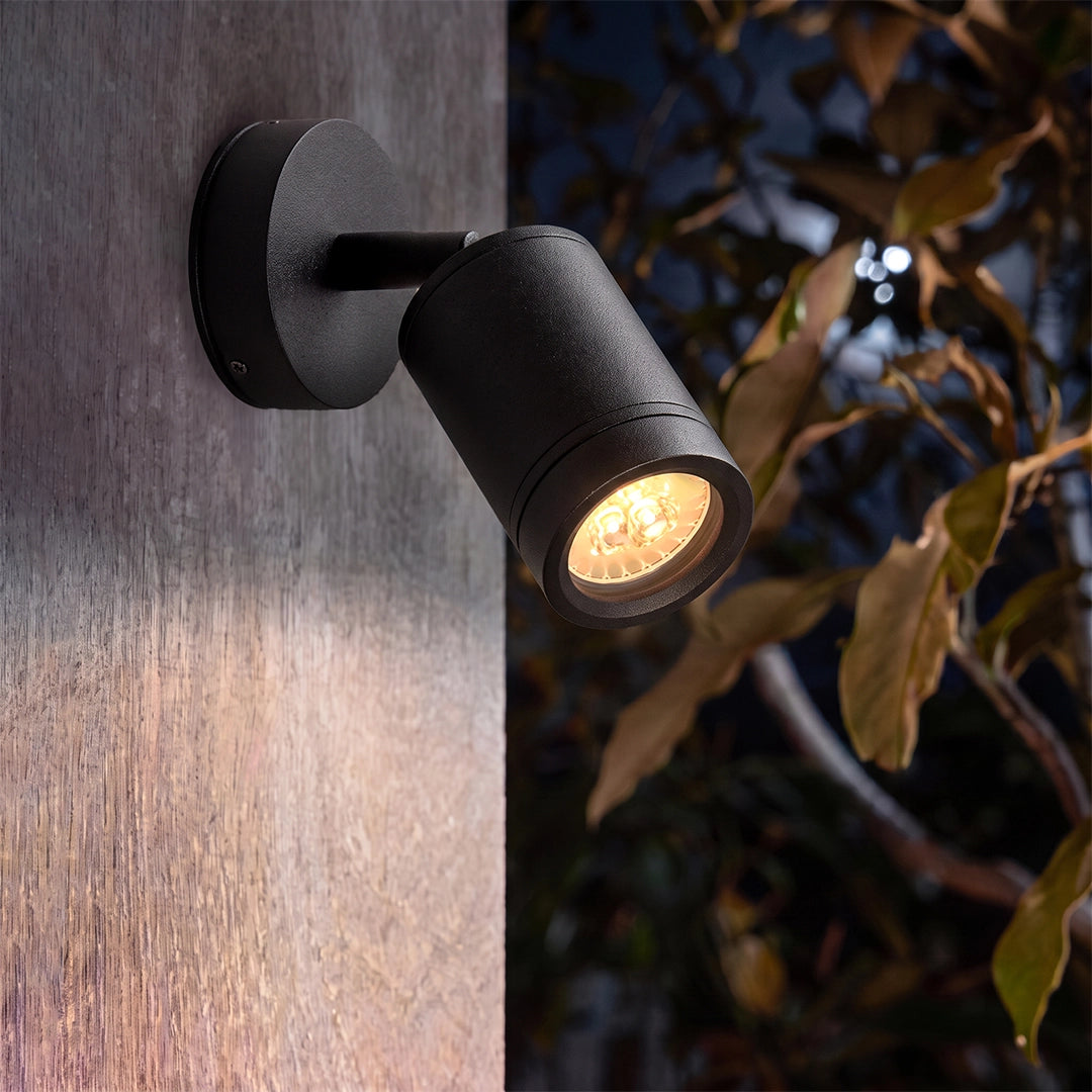 Close-up of a wall-mounted LED landscape spotlight with a black cylindrical head and warm beam.